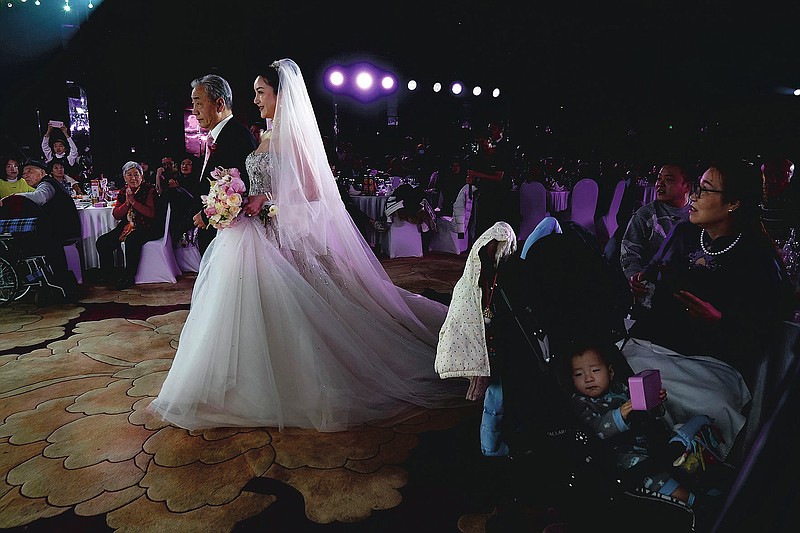 Bride Chen Yaxuan walks down the aisle with her father during an unmasked wedding banquet in Beijing on Saturday, Dec. 12, 2020. Lovebirds in China are embracing a sense of normalcy as the COVID pandemic appears to be under control in the country where it was first detected. (AP Photo/Ng Han Guan)