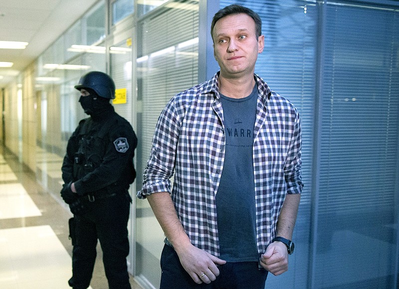 FILE- In this Dec. 26, 2019, file photo, Russian opposition leader Alexei Navalny speaks to the media in front of a security officer standing guard at the Foundation for Fighting Corruption office in Moscow, Russia. Russian authorities on Tuesday Dec. 29, 2020, ramped up pressure on top Kremlin critic Alexei Navalny, leveling new charges of fraud against him. (AP Photo/Alexander Zemlianichenko, File)