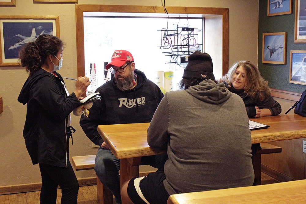 A waitress takes orders from unmasked customers at the Carver Hangar, a restaurant in Boring, Ore., on Jan. 6, 2021. As coronavirus deaths soar, a growing number of restaurants like Carver Hangar in states across the country are reopening in defiance of strict COVID-19 rules that have shut them down for indoor dining for weeks, or even months. “We’re not going to back down because our employees still need to eat, they still need that income,” said Bryan Mitchell, as customers ate at tables spaced 6 feet apart. (AP Photo/Gillian Flaccus)