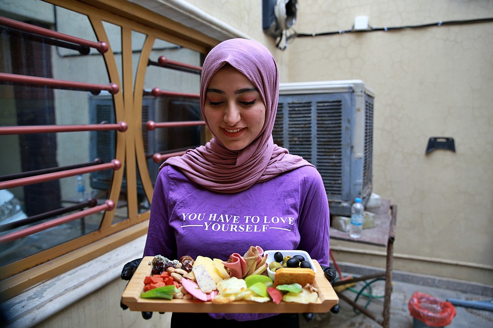 Fatima Ali shows her takeaway cheese-plate that she sells making a small but steady income, in Baghdad, Iraq, Saturday, Nov. 28, 2020. After Iraq imposed a coronavirus lockdown in March, Fatima is among a growing numbers of Iraqi women who are finding some good under the movement restrictions imposed because of the pandemic: They're starting their own businesses from home. (AP Photo/Khalid Mohammed)