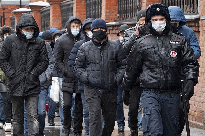 FILE - In this April 2, 2020, file photo, a policeman, foreground, accompanies a group of migrant laborers, who came to renew work permits, to a migration centre in St. Petersburg, Russia. A new U.N. report announced on Friday, Jan. 15, 2021, estimates that the COVID-19 pandemic reduced the number of international migrants by 2 million by the middle of 2020 because of border closings and a halt to travel worldwide — an estimated 27% decrease in expected growth. (AP Photo/Dmitri Lovetsky, File)