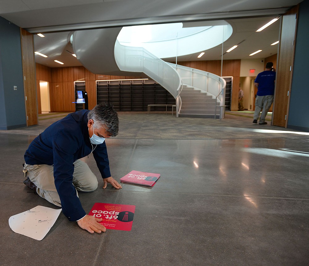 Sam Palmer, director of facilities and sustainability at the Fayetteville Public Library, applies decals Tuesday reminding library patrons of social-distancing expectations on the first day that the library has been open since its renovation and expansion. Voters in 2016 approved a property tax increase to help pay for the nearly $50 million expanded library's construction, which brings the building's size up to about 170,500 square feet. Library administrators opened to the public for the first time since late September, limiting the number of patrons to 200 at a time out of concern for the coronavirus pandemic. Visit nwaonline.com/210120Daily/ for today's photo gallery. 
(NWA Democrat-Gazette/Andy Shupe)