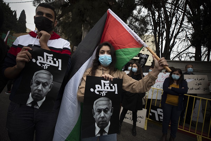 Palestinian protesters hold signs and flags during a demonstration against a visit of Israeli Prime Minister Benjamin Netanyahu to the northern Arab city of Nazareth, Israel, Wednesday, Jan. 13, 2021. Netanyahu, who has spent much of his long career casting Israel's Arab minority as a potential fifth column led by terrorist sympathizers, is now openly courting their support as he seeks reelection in the country's fourth vote in less than two years. (AP Photo/Sebastian Scheiner)