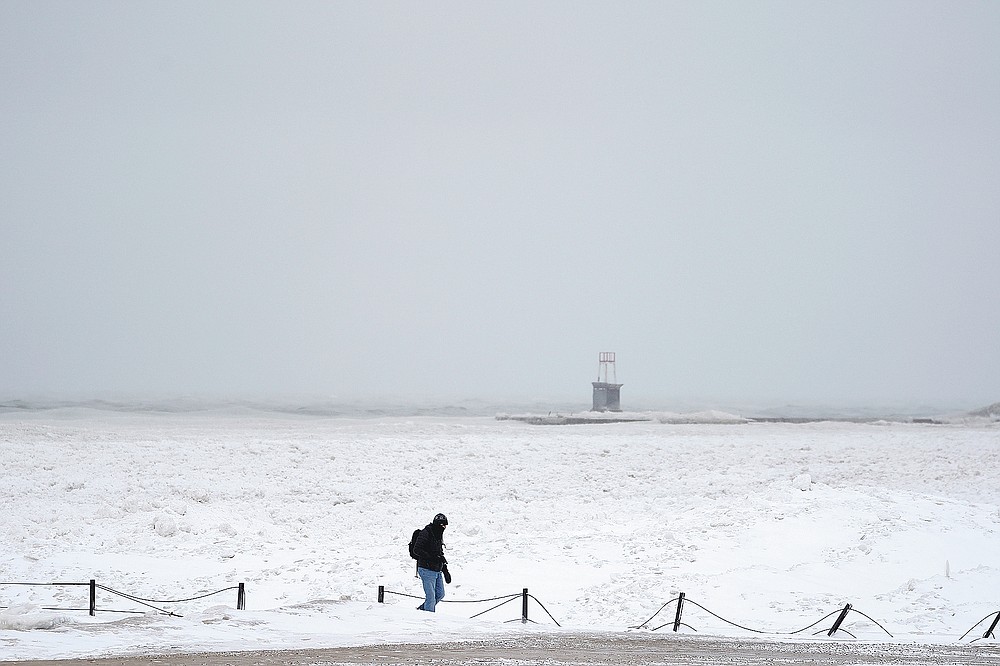 A lone man walks along a frozen section of North Ave. beach on Lake Michigan north of downtown Chicago Tuesday, Jan. 26, 2021. A major winter storm dumped more than a foot of snow on parts of the middle of the country stretching from central Kansas northeast to Chicago and southern Michigan.(AP Photo/Charles Rex Arbogast)