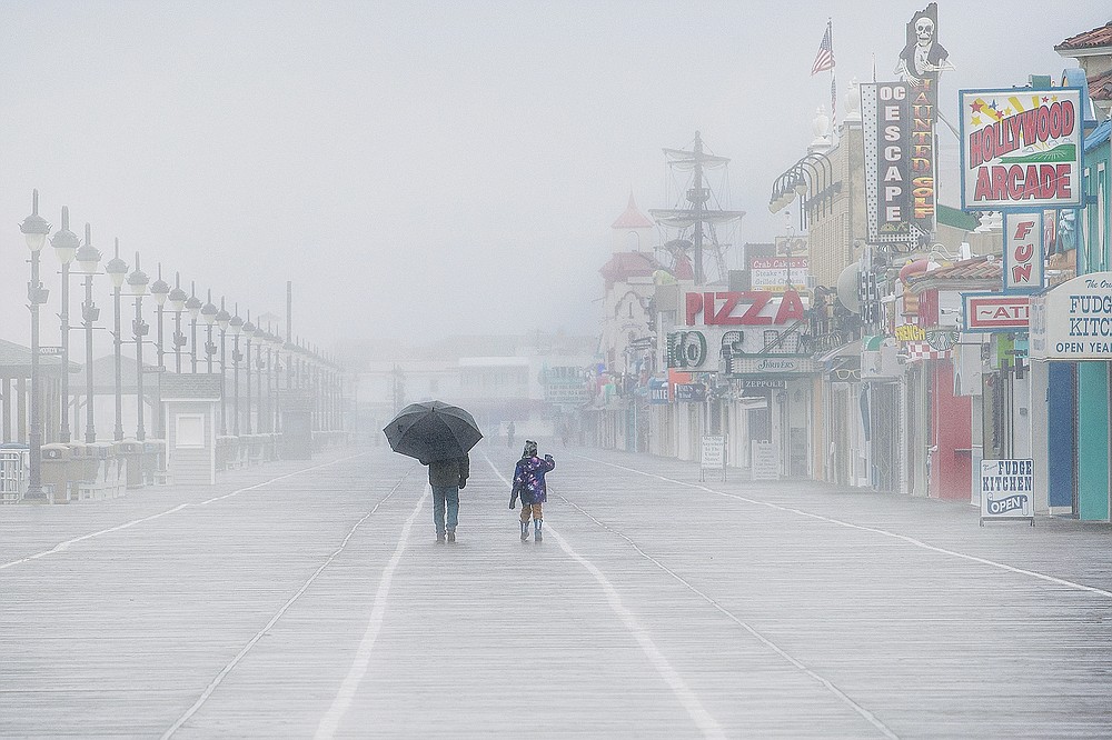 A man shields himself from the rain with an umbrella as he walks along with a child during a rainy and foggy winter afternoon at the Ocean City boardwalk in Ocean City, N.J. (Jose F. Moreno/The Philadelphia Inquirer via AP)