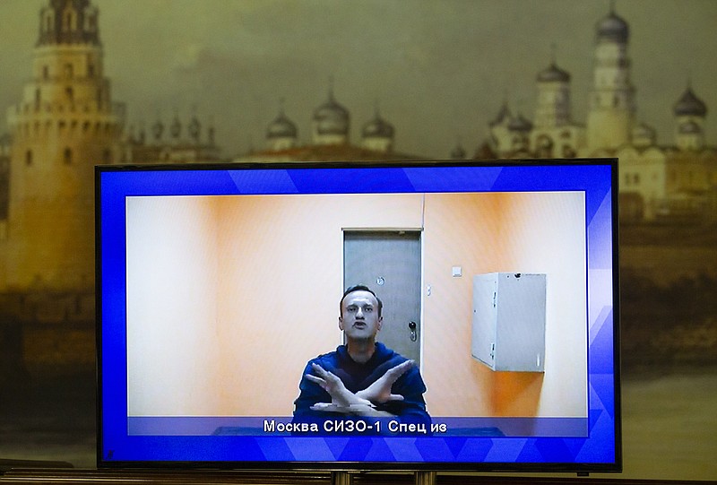 Russian opposition leader Alexei Navalny appears on a TV screen during a live session with the court during a hearing of his appeal in a court in Moscow, Russia, Thursday, Jan. 28, 2021, with an image of the Moscow Kremlin in the background. Navalny was jailed soon after arriving to Moscow after authorities accused him of violating of the terms of his 2014 fraud conviction. A court on Thursday is to hear an appeal on the ruling to remand him into custody. Next week, another court will decide whether to send him to prison for several years for the alleged violations. (AP Photo/Alexander Zemlianichenko)