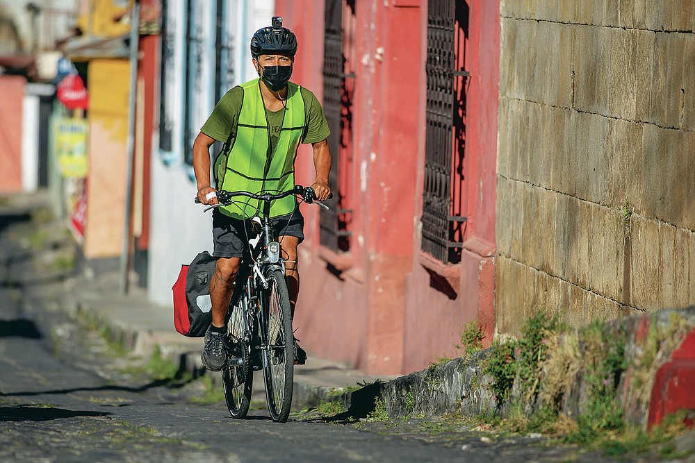Bonifaz Diaz rides through the streets of Quetzaltenango, Guatemala, Saturday, Jan. 30, 2021. Diaz has pedaled thousands of miles to carry books that people can barter for bags of a cereal mix aimed at providing relief to families suffering chronic malnutrition. (Henning Sac via AP)