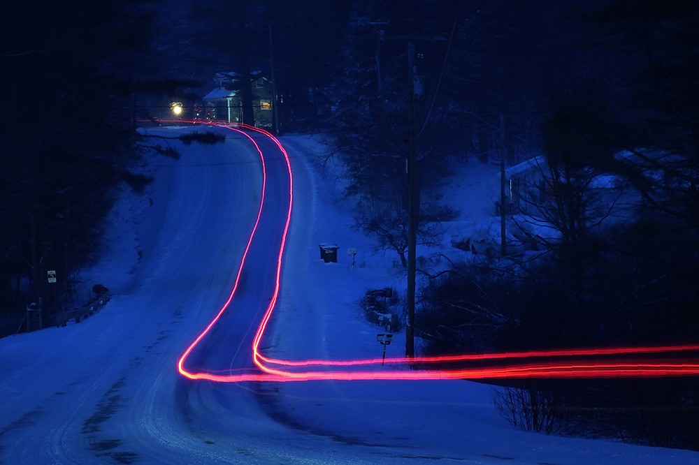 In this photo taken with a long exposure, a car driven on a snow-covered road leaves a trail of light during a winter snow storm, Tuesday morning, Feb. 2, 2021, in Freeport, Maine. (AP Photo/Robert F. Bukaty)