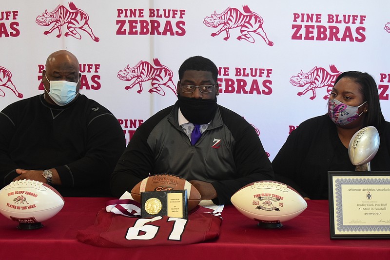 Pine Bluff High School defensive tackle Braylon Clark, center, finishes signing his letter of intent with the University of Central Arkansas on Wednesday at the high school's Student Center. He is flanked by his father, Richard Clark, and his mother, Loretta Givens. (Pine Bluff Commercial/I.C. Murrell)