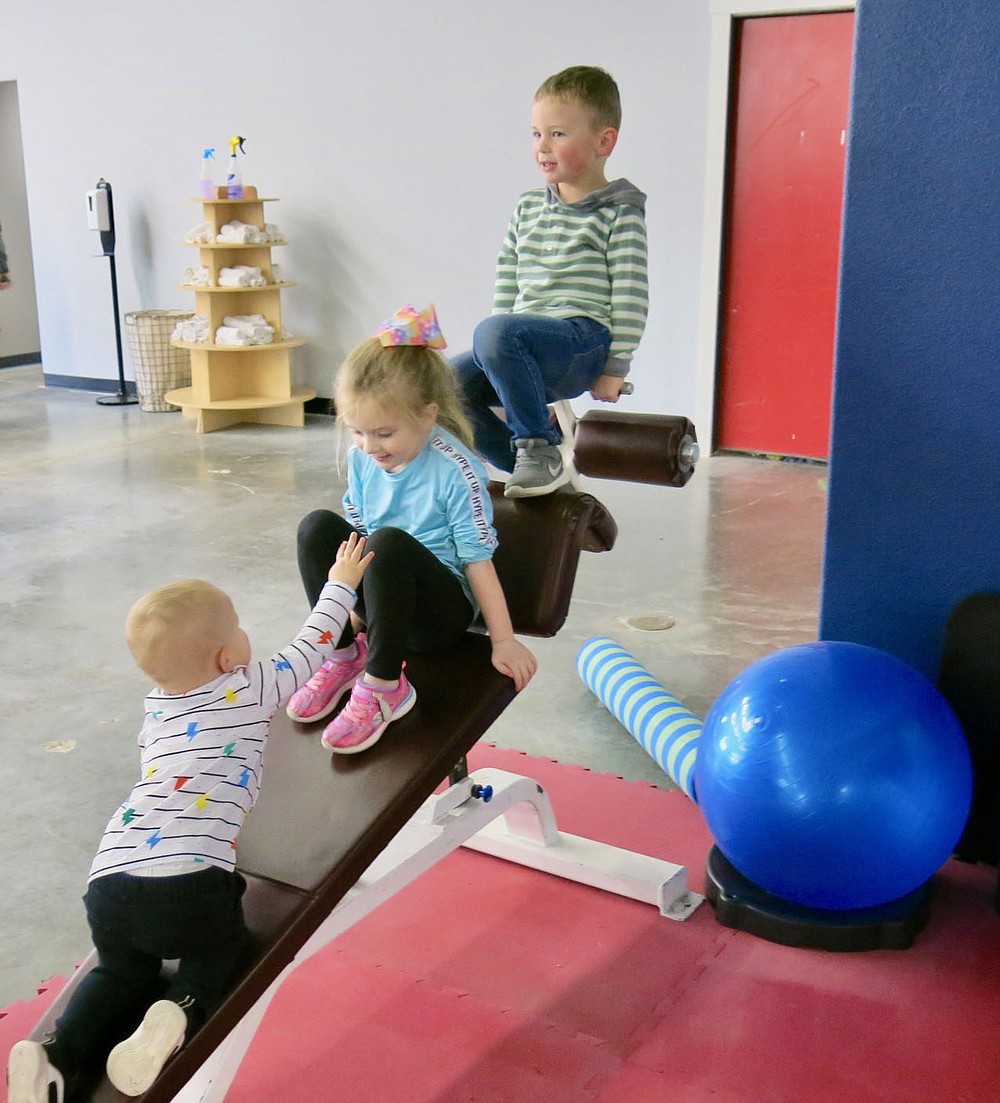 Westside Eagle Observer/SUSAN HOLLAND
Young Bryce Riddle, almost 2, reaches out to Kaylee McCormick, of Siloam, as his brother, Weston, 4, sits above her. The youngsters were enjoying the exercise equipment at the Gravette Gym during its grand opening Saturday, Feb. 6. Bryce and Weston are sons of the gym owners, Les and Natanya Riddle.