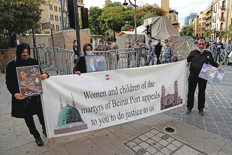 Relatives of victims of the Aug. 4 Beirut port explosion hold a banner and portraits of their loved ones who died in the explosion, during a sit-in near the Parliament building to demand an expedited investigation, in Beirut, Lebanon, Wednesday, Nov. 25, 2020. The blast was one of the largest non-nuclear explosions in history and six months later, political and confessional rivalries have undermined the probe into the Beirut port explosion and brought it to a virtual halt, mirroring the same rivalries that have thwarted past attempts to investigate political crimes throughout Lebanon's history. (AP Photo/Hussein Malla)