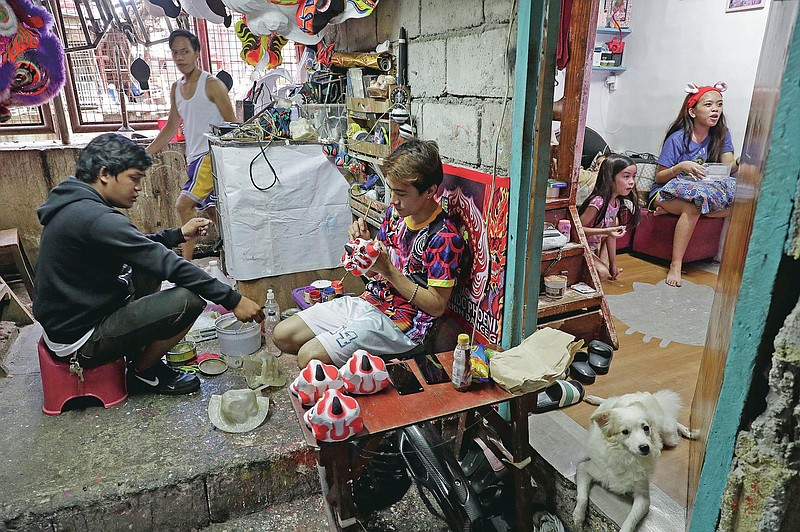 Therry Sicat, center, finishes paint on miniature lion heads as they seek other ways to earn a living at a creekside slum at Manila's Chinatown, Binondo Philippines on Feb. 3, 2021. The Dragon and Lion dancers won't be performing this year after the Manila city government has banned the dragon dance, street parties, stage shows or any other similar activities during celebrations for the Chinese New Year due to COVID-19 restrictions leaving several businesses without income as the country grapples to start vaccination this month. (AP Photo/Aaron Favila)
