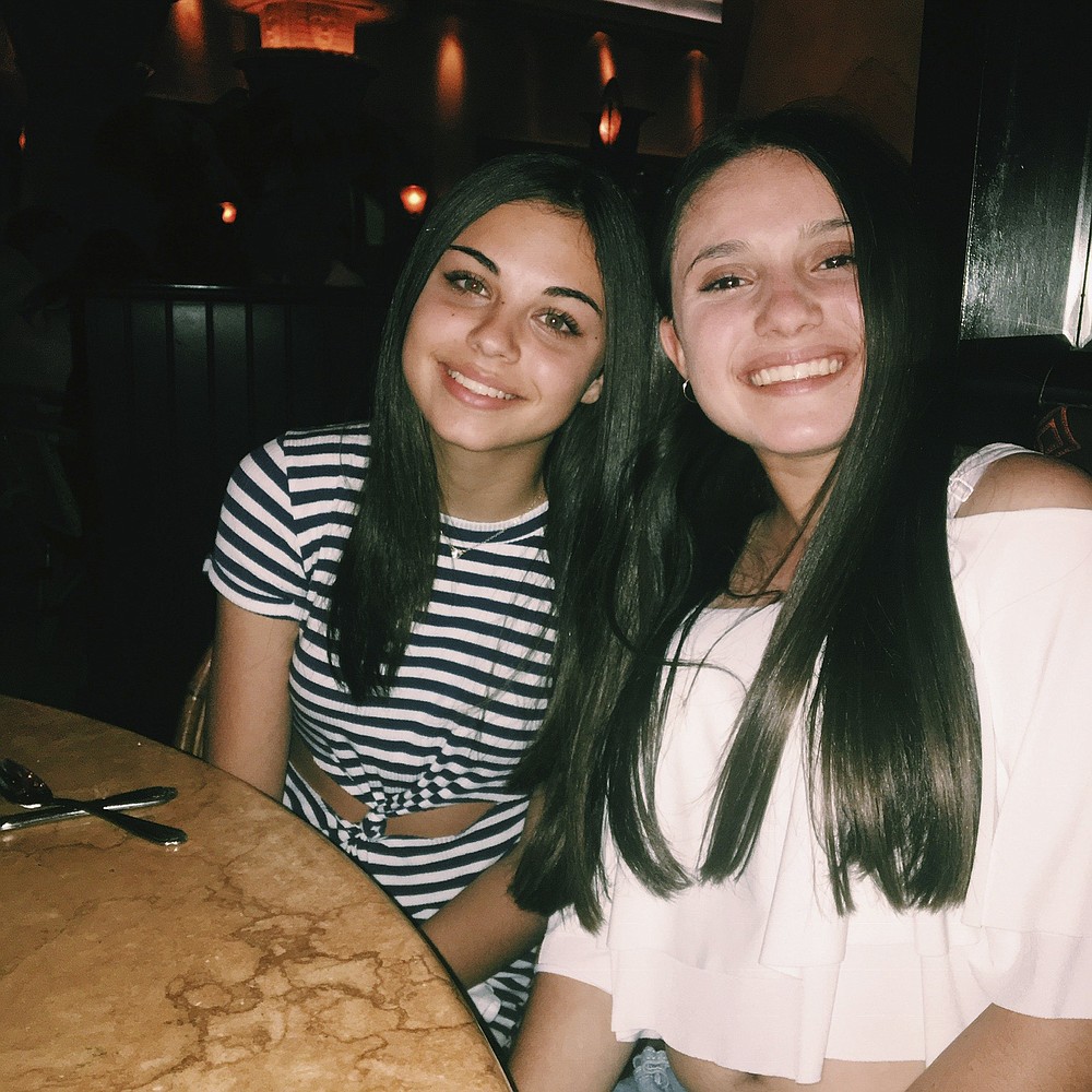 In this undated photo made available by Lori Alhadeff, her daughter Alyssa, right, sits at a table with her best friend Abby Price. Alyssa was killed in the 2018 Valentine's Day massacre at Marjory Stoneman Douglas High School in Parkland, Fla. Abby's family moved to North Carolina for her junior year hoping for a fresh start. She was terrified of a new school, forging new friendships and then COVID hit, marring the rest of her high school experience. (Lori Alhadeff via AP)