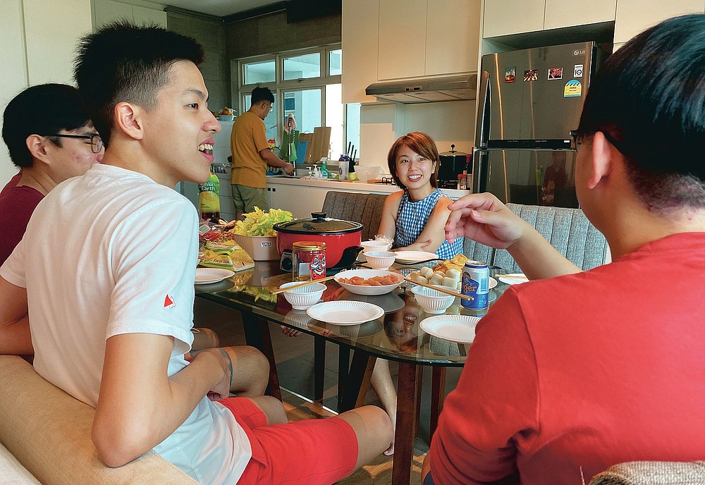 Chan Jit Yen smiles as she hosts Malaysian students, foreground, during a Lunar New Year hot pot lunch at her rented apartment in Singapore Saturday, Feb. 13, 2021. With Malaysian workers and students stranded in the city state over the Lunar New Year due to coronavirus travel restrictions, the Malaysian Association in Singapore has called on Malaysians to treat students to a meal. (AP Photo/Annabelle Liang)