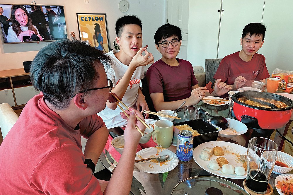 Malaysian students, from left, Felix Mong, Jason Ong, Ter Leong Kern and Siew Ee Sung eat bak kwa, a Chinese meat product similar to jerky, during a Lunar New Year hot pot lunch hosted by a Malaysian couple at their rented apartment in Singapore, Saturday, Feb. 13, 2021. With Malaysian workers and students stranded in the city state over the Lunar New Year due to coronavirus travel restrictions, the Malaysian Association in Singapore has called on Malaysians to treat students to a meal. (AP Photo/Annabelle Liang)
