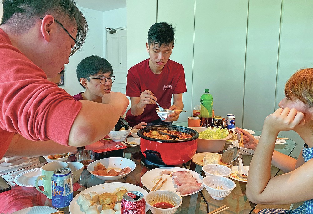 Malaysian students, from left, Felix Mong, Ter Leong Kern and Siew Ee Sung enjoy a Lunar New Year hot pot lunch provided by their Malaysian host Chan Jit Yen, right, at her rented apartment in Singapore, Saturday, Feb. 13, 2021. With Malaysian workers and students stranded in the city state over the Lunar New Year due to coronavirus travel restrictions, the Malaysian Association in Singapore has called on Malaysians to treat students to a meal. (AP Photo/Annabelle Liang)