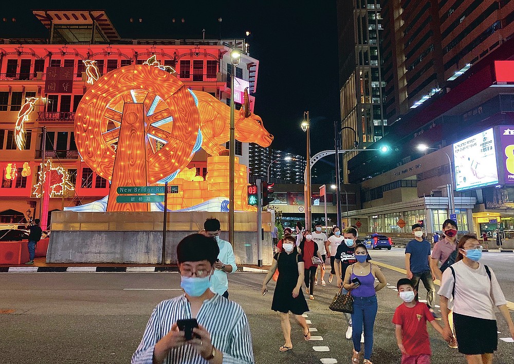 Pedestrians cross a street with a lit giant ox display to welcome the Lunar New Year at Chinatown in Singapore in Singapore Friday, Feb. 12, 2021. With Malaysian workers and students stranded in the city state over the Lunar New Year due to coronavirus travel restrictions, the Malaysian Association in Singapore has called on Malaysians to treat students to a meal. (AP Photo/Annabelle Liang)