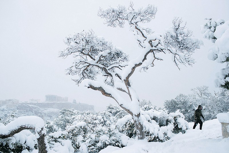 A man walks at Filopapos hill as snow falls, with the ancient Acropolis hill and the Parthenon temple, in background, Athens, on Tuesday, Feb. 16, 2021. There have been record subzero temperatures in Texas and Oklahoma, and Greenland is warmer than normal. Snow fell in Greece and Turkey. Meteorologists blame the all-too-familiar polar vortex. (AP Photo/Petros Giannakouris)