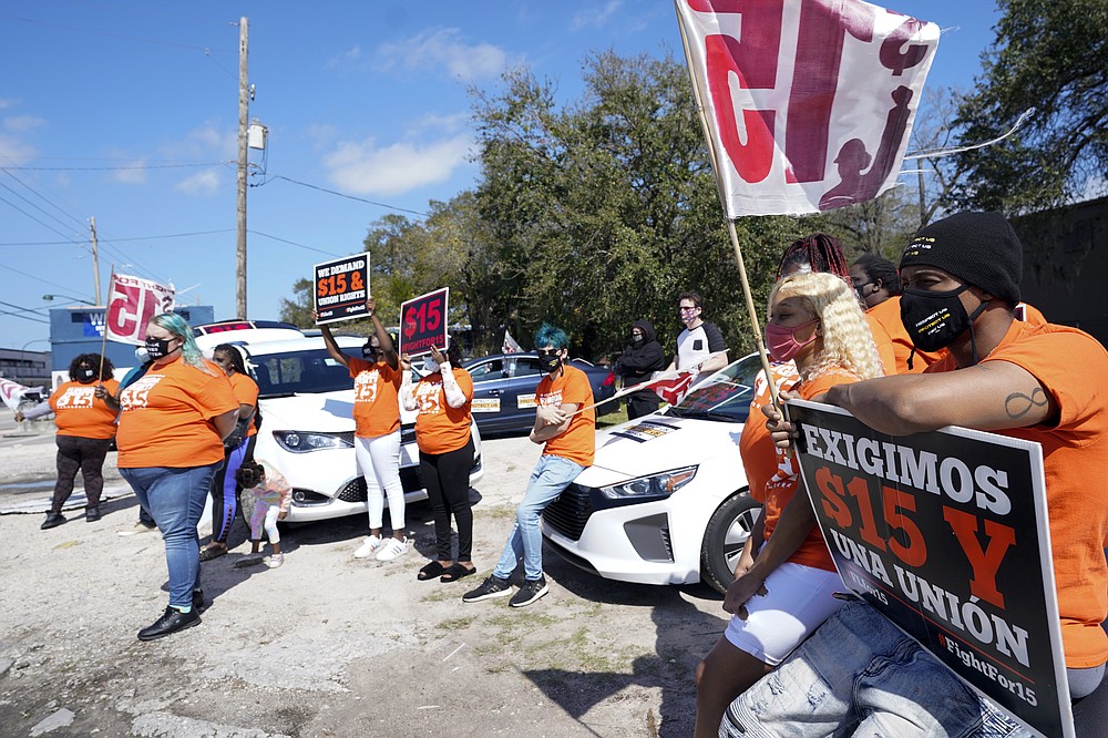 Cristian Cardona, sitting on a car hood, center, an employee at a McDonald's, attends a rally for a $15 an hour minimum wage Tuesday, Feb. 16, 2021, in Orlando, Fla. (AP Photo/John Raoux)