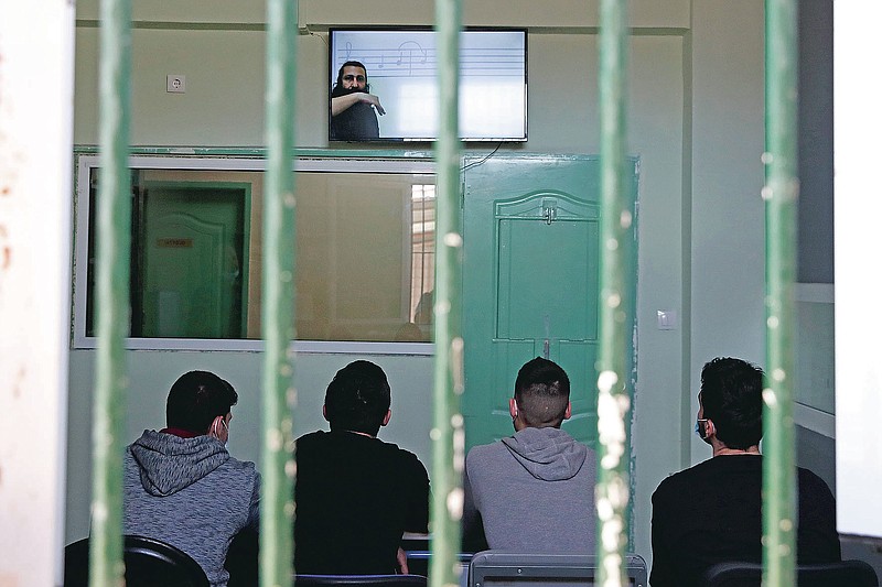 Inmates sitting inside a room, watch a recorded music lesson in Avlona prison, north of Athens, Wednesday, Feb. 10, 2021. With Greece's schools shut due to the pandemic, all lessons have gone online. But the online world isn't within reach of everyone _ and particularly not within reach of the students of Avlona Special Youth Detention Center, where internet devices are banned by law from the cells. (AP Photo/Thanassis Stavrakis)