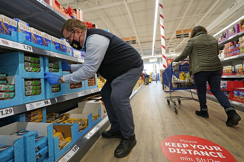 In this Thursday, Feb. 4, 2021 photo, grocery supervisor Joseph Lupo, left, arranges cookies in the shelves at the Lidl food market in Lake Grove, N.Y., where he works after getting the first dose of the COVID-19 vaccination earlier in the day. Lupo, who fell ill with the virus in March, was elated to get his first vaccine dose. "I never ever want to get COVID again, or see anybody else get it," said Lupo, 59. (AP Photo/Kathy Willens)