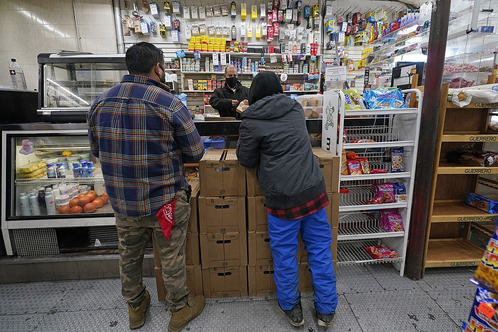 Bodega owner Francisco Marte helps two customers Wednesday, Feb. 10, 2021, at his small grocery store in the Bronx borough of New York. Marte, president of the Bodega and Small Business Group, which represents bodegas in New York, has been lobbying local officials to set aside vaccine appointments for bodega workers, many of whom are unaware they are eligible. He hopes that the recent opening of a large vaccination site at Yankee stadium will make access easier. (AP Photo/Kathy Willens)