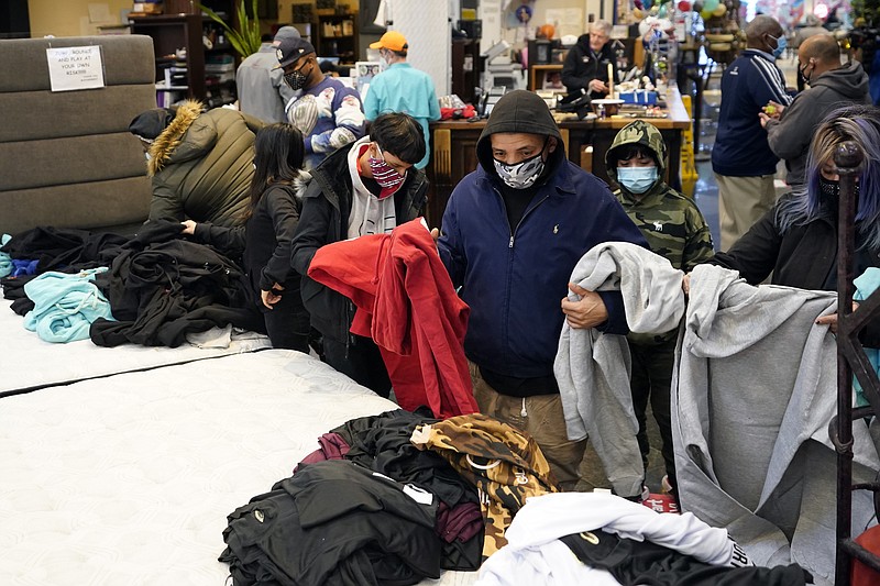 FILE - In this Feb. 16, 2021, file photo, people select shirts and sweatshirts being given away at a Gallery Furniture store after the owner opened his business as a shelter for those without power at their homes in Houston. Making decisions about risks — large or small — in the pandemic era is fraught enough. But the storms and outages ravaging Texas and other states have added a whole new layer to the process. (AP Photo/David J. Phillip, File)