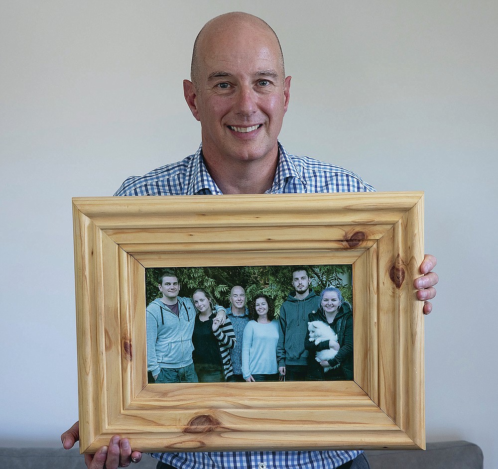 Jonathan Manning holds a photo of his children and their partners at his home in Christchurch, New Zealand, Wednesday, Feb. 10, 2021. Manning helped guide his teenage children through their grief after their mother Donna Manning was killed. One woman has used her anger to ensure buildings are safer. Others have found peace after heartbreaking losses. Ten years after an earthquake in Christchurch killed 185 people and devastated the city, some of those profoundly affected are sharing their journeys. (AP Photo/Peter Meecham)