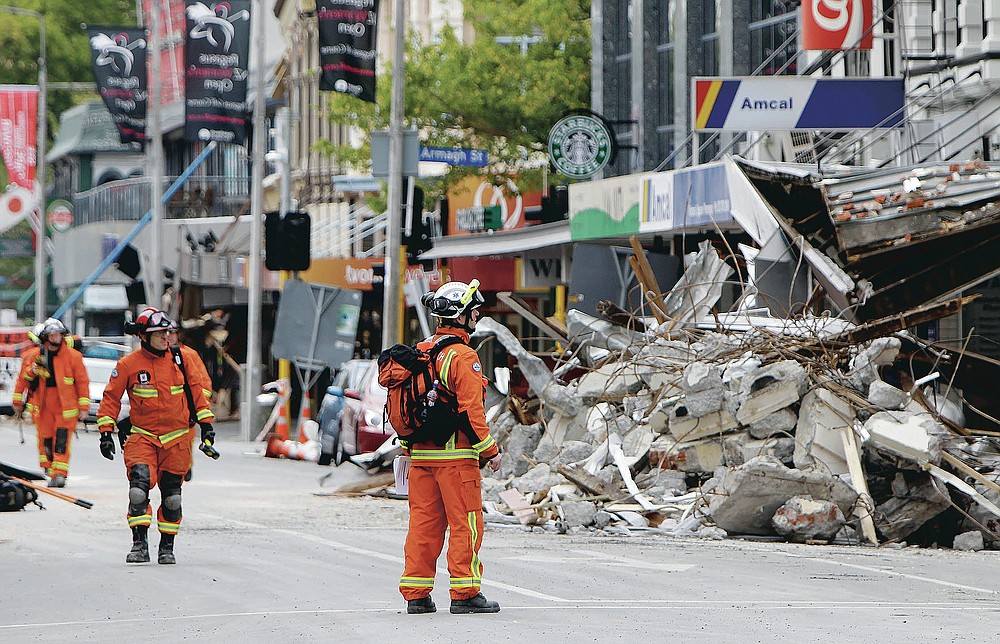 FILE - In this Feb. 26, 2011, file photo, representatives from the United Kingdom Fire and Rescue Service inspect the earthquake-damaged buildings in Colombo Street, Christchurch, New Zealand. One woman has used her anger to ensure buildings are safer. Others have found peace after heartbreaking losses. Ten years after the earthquake in Christchurch killed 185 people and devastated the city, some of those profoundly affected are sharing their journeys. (AP Photo/Mark Baker, File)
