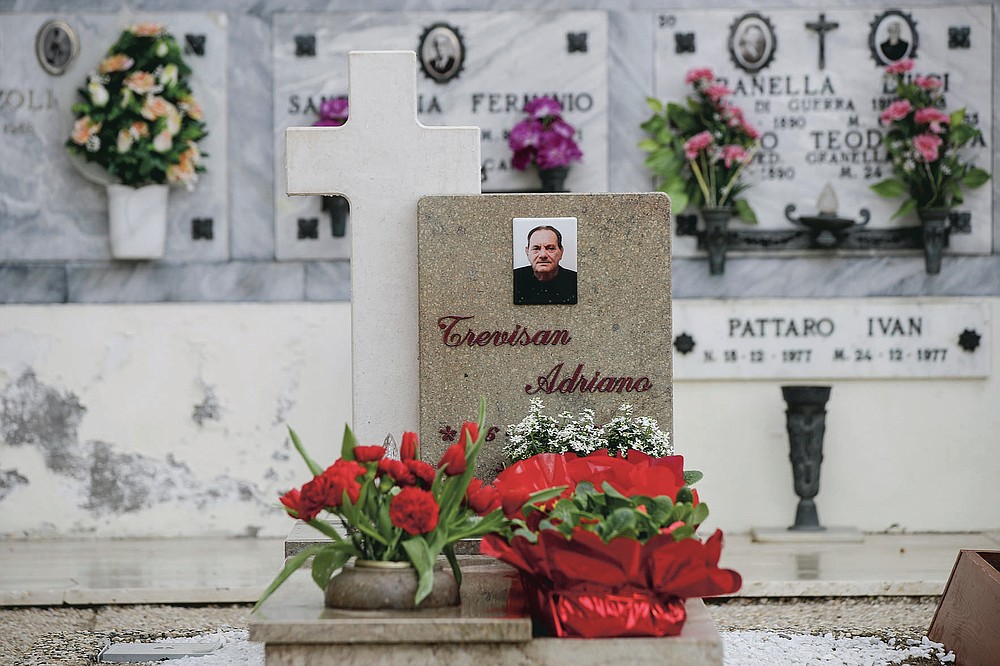Flowers adorn the tombstone of Adriano Trevisan, Italy's first known victim of COVID-19, at the cemetery of Vo Vecchio, in Vo Euganeo, Italy, Wednesday, Feb. 10, 2021. Shockwaves ran through the wine-making village of Vo', west of Venice, as word spread last Feb. 21 that a retired roofer had died of the new coronavirus becoming the first known COVID-19 victim in the West. (AP Photo/Luca Bruno)