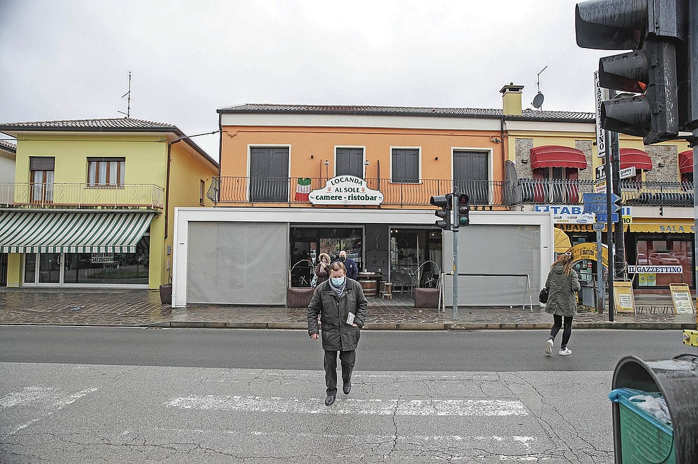 People walk in front of a cafè in Vo Euganeo, northern Italy, Wednesday, Feb. 10, 2021. Shockwaves ran through the wine-making village of Vo, west of Venice, as word spread last Feb. 21 that a retired roofer had died of the new coronavirus becoming the first known COVID-19 victim in the West. (AP Photo/Luca Bruno)