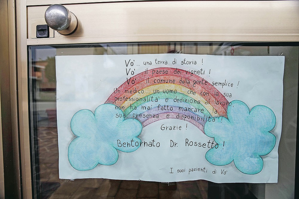 A poster made by patients hangs on the door of doctor Luca Rossetto's medical office in Vo Euganeo, northern Italy, Wednesday, Feb. 10, 2021. Shockwaves ran through the wine-making village of Vo, west of Venice, as word spread last Feb. 21 that a retired roofer had died of the new coronavirus becoming the first known COVID-19 victim in the West. Writing on poster reads in Italian; "Vo... a land of history! Vo'...a town of vineyards! Vo'...the council of simple people! A doctor...a man...who with his professionalism and dedication to work never missed his presence and availability! Thank you! Welcome Dr. Rossetto!" (AP Photo/Luca Bruno)
