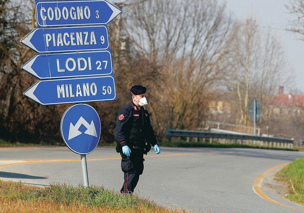 FILE - In thisMonday, Feb. 24, 2020 file photo, a Carabinieri (Italian paramilitary police) officer checks transit to or from the cordoned area in Codogno, some 50 kilometers South-East of Milan, Italy. Italy delivered the first shocking confirmation of locally transmitted coronavirus infections outside of Asia a year ago Sunday, with back-to-back revelations of cases more than 150 kilometers (nearly 100 miles) apart in the country's north. First, a 38-year-old man in Codogno, an industrial town in the Lombardy region, tested positive for COVID-19, sending panicked residents to pick up their children from school, stock up on provisions at grocery stores and search in vain for surgical masks at pharmacies. (AP Photo/Antonio Calanni, File)