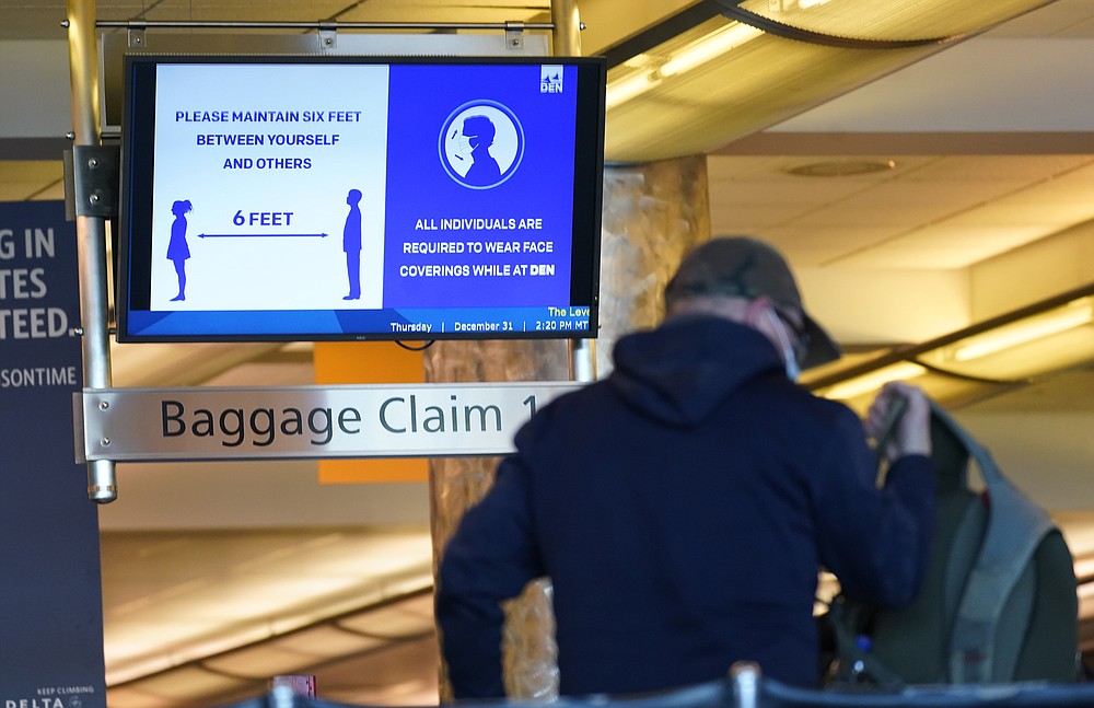 FILE - In this Dec. 31, 2020, file photo, an electronic sign advises travelers to wear face masks and practice social distancing while passing through the main terminal of Denver International Airport in Denver. At least for now, U.S. health authorities say after being vaccinated, people should follow the same rules as everybody else about wearing a mask, keeping a 6-foot distance and avoiding crowds even after they’ve gotten their second vaccine dose. (AP Photo/David Zalubowski, File)