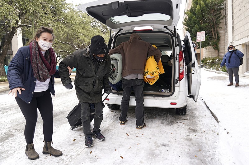 FILE - In this Feb. 16, 2021 file photo, Morgan Handley, left, helps move people to a warming shelter at Travis Park Methodist Church to help escape sub-freezing temperatures, in San Antonio.  With the snow and ice clearing in Texas after the electricity was cut to millions as temperatures plunged, people are being found who likely froze to death as they struggled to stay warm in their unheated homes. (AP Photo/Eric Gay, File)