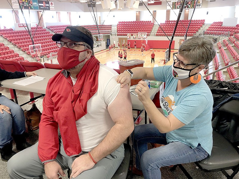 LYNN KUTTER ENTERPRISE-LEADER
The weather cleared up just in time Saturday for Farmington School District employees to receive their second Pfizer covid-19 vaccine at Cardinal Arena. While the girls basketball team practices in the background, Jodi Hendricks with the school gives a covid-19 shot to Adam Simmons, assistant senior high basketball ball coach. Prairie Grove school employees already have received their second vaccinations and Lincoln Consolidated School District will have their second clinic later this month.