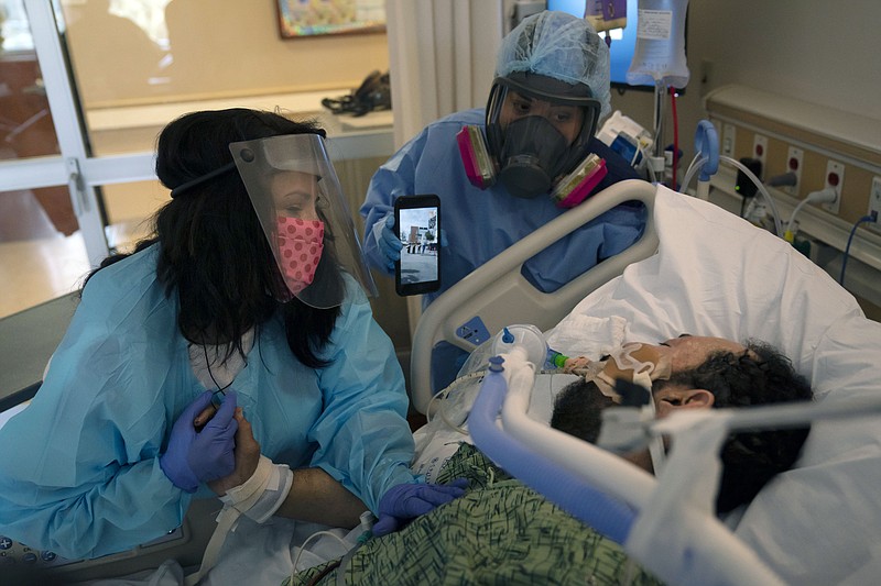 The Associated Press
In this Feb. 15 file photo, Patty Trejo, 54, left, looks at her intubated husband, Joseph, in a COVID-19 unit as registered nurse Celina Mande holds a smartphone showing a mariachi band performing for the patient at St. Jude Medical Center, in Fullerton, Calif. Trejo visited her husband for the first time since he was hospitalized more than a month ago. A survivor of COVID-19 herself, she invited a mariachi band to give him courage. Surrounded by hospital staff, family members and friends in the parking lot of the hospital, the band played her husband's favorite song, "La mano de Dios," or "The Hand of God." "He needs to know that I still love him, and he needs to know he's got to fight," said Trejo.