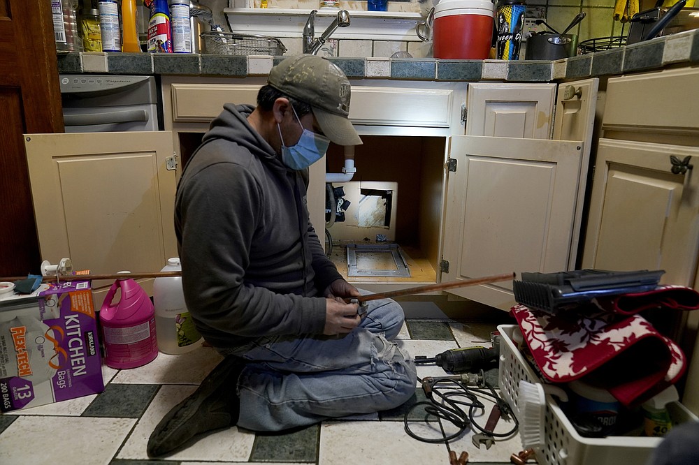 CORRECTING LAST NAME TO VALERIO, NOT VALERIA - Craftsman Roberto Valerio is working in Dallas on Saturday February 20, 2021 repairing a broken pipe under the sink at Nora Espinoza's home.  The pipe broke in sub-zero temperatures caused by last week's winter weather.  (AP Photo / Tony Gutierrez)