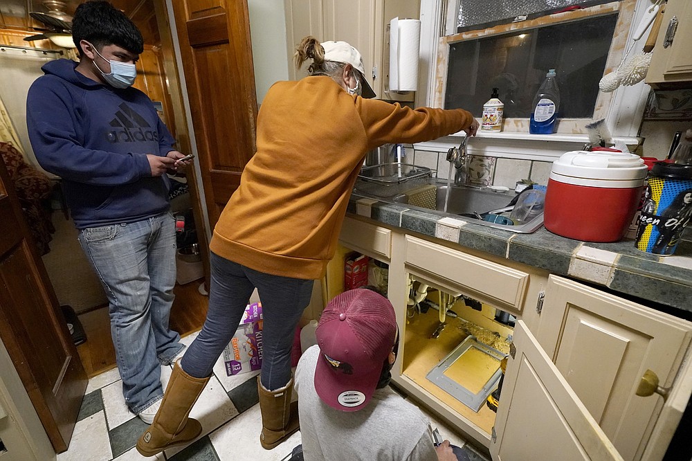 CORRECTING THE LAST NAME TO VALERIO, NOT VALERIA - Roberto Valerio Jr. (left) and his cousin Hector Valerio (right), as homeowner Nora Espinoza, watch water leaking from the tap after a repair was carried out on a broken pipe below Sink, Saturday, February 20, 2021, in Dallas.  There were several burst pipes in Espinoza's house in freezing temperatures caused by last week's winter weather.  (AP Photo / Tony Gutierrez)