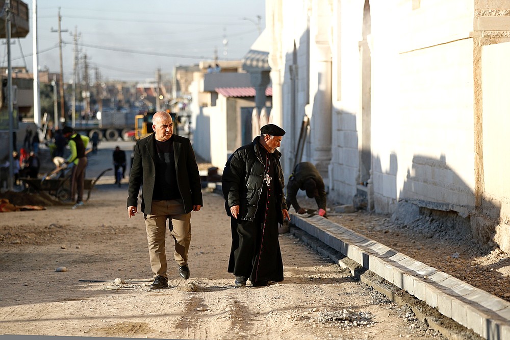 A priest watches workers fix a street destroyed during clashes against the Islamic State militants in Qaraqosh, Iraq, Tuesday, Feb. 23, 2021. Iraq's Christians are hoping that a historic visit by Pope Francis in March will help boost their community's struggle to survive. The country's Christian population has been dwindling ever since the turmoil that followed the 2003 U.S.-led invasion. And it was dealt a near death blow in 2014, when Islamic State group militants overran northern Iraq, site of Iraq's historical Christian heartland. (AP/Photo/Hadi Mizban)