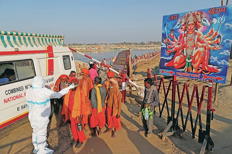 A health worker takes nasal swab samples of Hindu holy men, to test for COVID-19 next to a poster of Hindu God Hanuman during Magh Mela festival, in Prayagraj, India. Wednesday, Feb. 24, 2021. Millions of people have joined a 45-day long Hindu bathing festival in this northern Indian city, where devotees take a holy dip at Sangam, the sacred confluence of the rivers Ganga, Yamuna and the mythical Saraswati. Here, they bathe on certain days considered to be auspicious in the belief that they be cleansed of all sins. (AP Photo/Rajesh Kumar Singh)