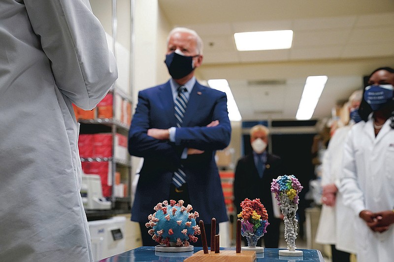 FILE - In this Thursday, Feb. 11, 2021 file photo, President Joe Biden visits the Viral Pathogenesis Laboratory at the National Institutes of Health (NIH) in Bethesda, Md. At bottom center is a model of the COVID-19 virus. On Friday, Feb. 26, 2021, The Associated Press reported on stories circulating online incorrectly asserting Biden restored taxpayer funding for the Wuhan Institute of Virology. Social media users are falsely claiming the Biden administration is bankrolling the Wuhan Institute of Virology, a Chinese lab which has faced unproven allegations that the coronavirus leaked from the facility leading to the global COVID-19 pandemic. (AP Photo/Evan Vucci)