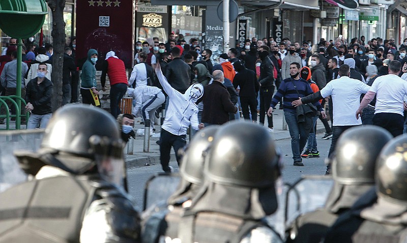 Protestors throw stones at the riot police during a protest, in a street in Skopje, North Macedonia, on Friday, Feb. 26, 2021. Several hundred people, including relatives of convicted in a recent court verdict on the fishermen murder, have clashed with strong police forces on Friday, with reports of injured police officers. (AP Photo/Boris Grdanoski)