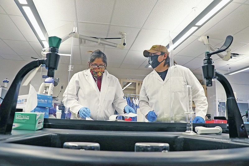 This undated image provided by Navajo Technical University shows Robinson Tom, right, assisting general education graduate Noelle Clark with a biology assignment at the university in Crownpoint, New Mexico. Tom worked as a lab assistant in the NTU Wet Labs upon graduation in May 2020. (Daniel Vandever, NTU, via AP)