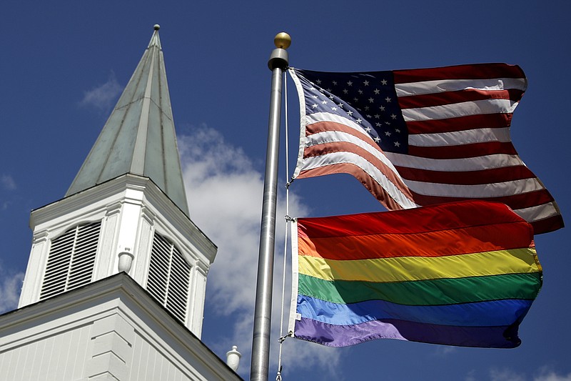 FILE - In this April 19, 2019 file photo, a gay pride rainbow flag flies along with the U.S. flag in front of the Asbury United Methodist Church in Prairie Village, Kan. Conservative leaders within the United Methodist Church unveiled plans Monday, March 1, 2021 to form a new denomination, the Global Methodist Church, with a doctrine that does not recognize same-sex marriage. The move could hasten the long-expected breakup of the UMC, America’s largest mainline Protestant denomination, over differing approaches to LGBTQ inclusion. (AP Photo/Charlie Riedel, File)