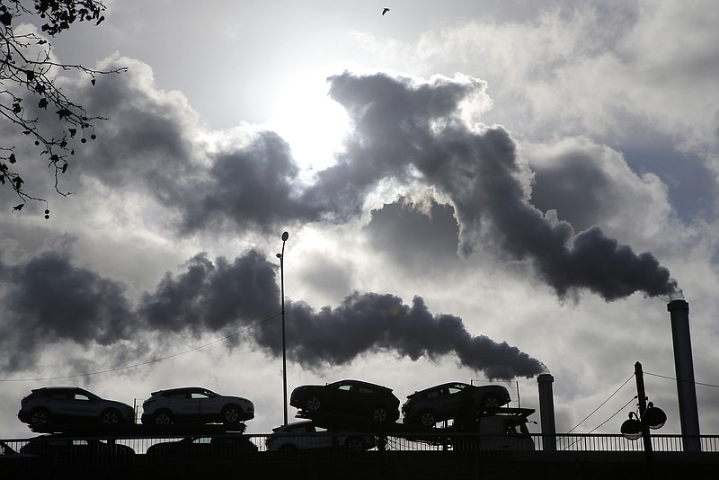 FILE - In this Friday, Nov. 30, 2018 file photo smoke rises from a factory as a truck loaded with cars crosses a bridge in Paris. Global energy-related carbon dioxide emissions rose slightly in December compared to the same month of 2019, indicating the sharp drop seen due to the pandemic was short-lived. Figures released Tuesday by the International Energy Agency show emissions from the production and use of oil, gas and coal were 2% higher in December 2020 than a year earlier. (AP Photo/Michel Euler, File)