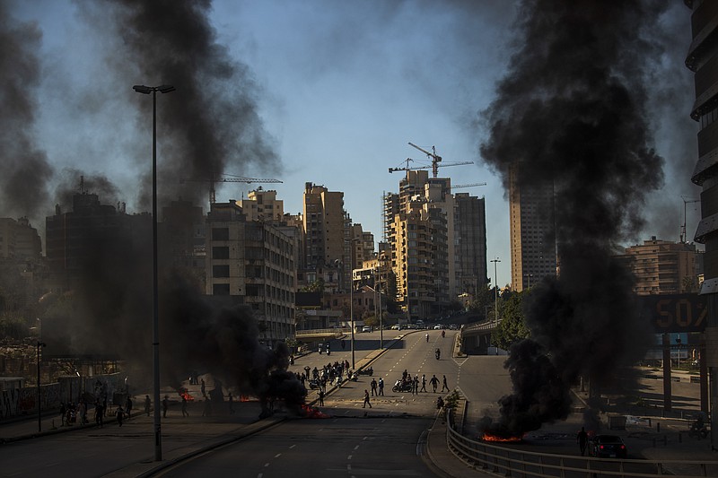 Protesters stand in front of burning tires set on fire to block a main road, after the Lebanese pound hit a record low against the dollar on the black market, in Beirut, Lebanon, Saturday, March 6, 2021. (AP Photo/Hassan Ammar)