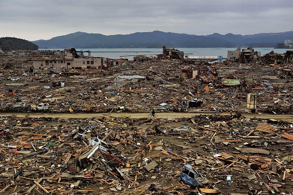 CORRECTION DATE - In this file photo dated March 15, 2011, a survivor of the earthquake and tsunami rides a bicycle through the flat city of Minamisanriku in northeastern Japan four days after the tsunami.  (AP Photo / David Guttenfelder, file)