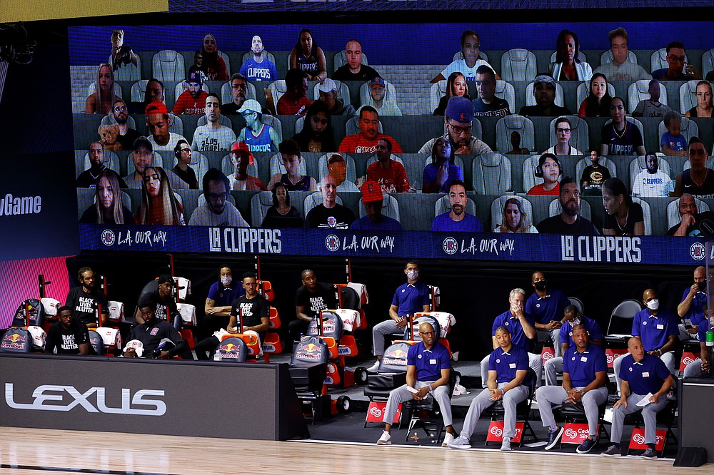 FILE - This Tuesday, Aug. 4, 2020, file photo shows a view of the Los Angeles Clippers bench and fans on a screen during the first half of an NBA basketball game against the Phoenix Suns in Lake Buena Vista, Fla. The entire essence of sports as we know them changed in subtle, if fundamental, ways during the past 12 months because of restrictions on crowds. (Kevin C. Cox/Pool Photo via AP, File)