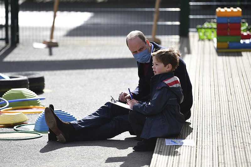Britain's Prince William talks with a child in the playground during a visit with Kate, Duchess of Cambridge to School21, a school in east London, Thursday March 11, 2021. Prince William has defended Britain’s monarchy against accusations of bigotry made by his brother, Prince Harry, and his sister-in-law, Meghan, insisting the family is not racist. In comments made during a visit Thursday to an east London school, William became the first royal to directly address the explosive interview his brother and Meghan gave to Oprah Winfrey. Buckingham Palace sought to respond to Harry and Meghan’s allegations of racism and mistreatment in a 61-word statement, but it has failed to quell the controversy. (Justin Tallis/Pool via AP)